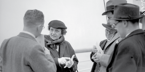 Black and white photo of Secretary of Labor Frances Perkins, the first woman in the U.S. Cabinet, addressing members of the press.