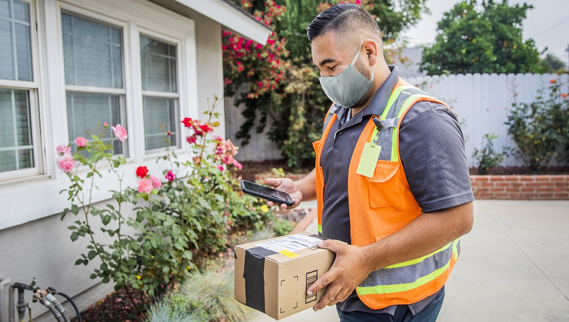 A male worker wearing a safety vest delivers a package to a home