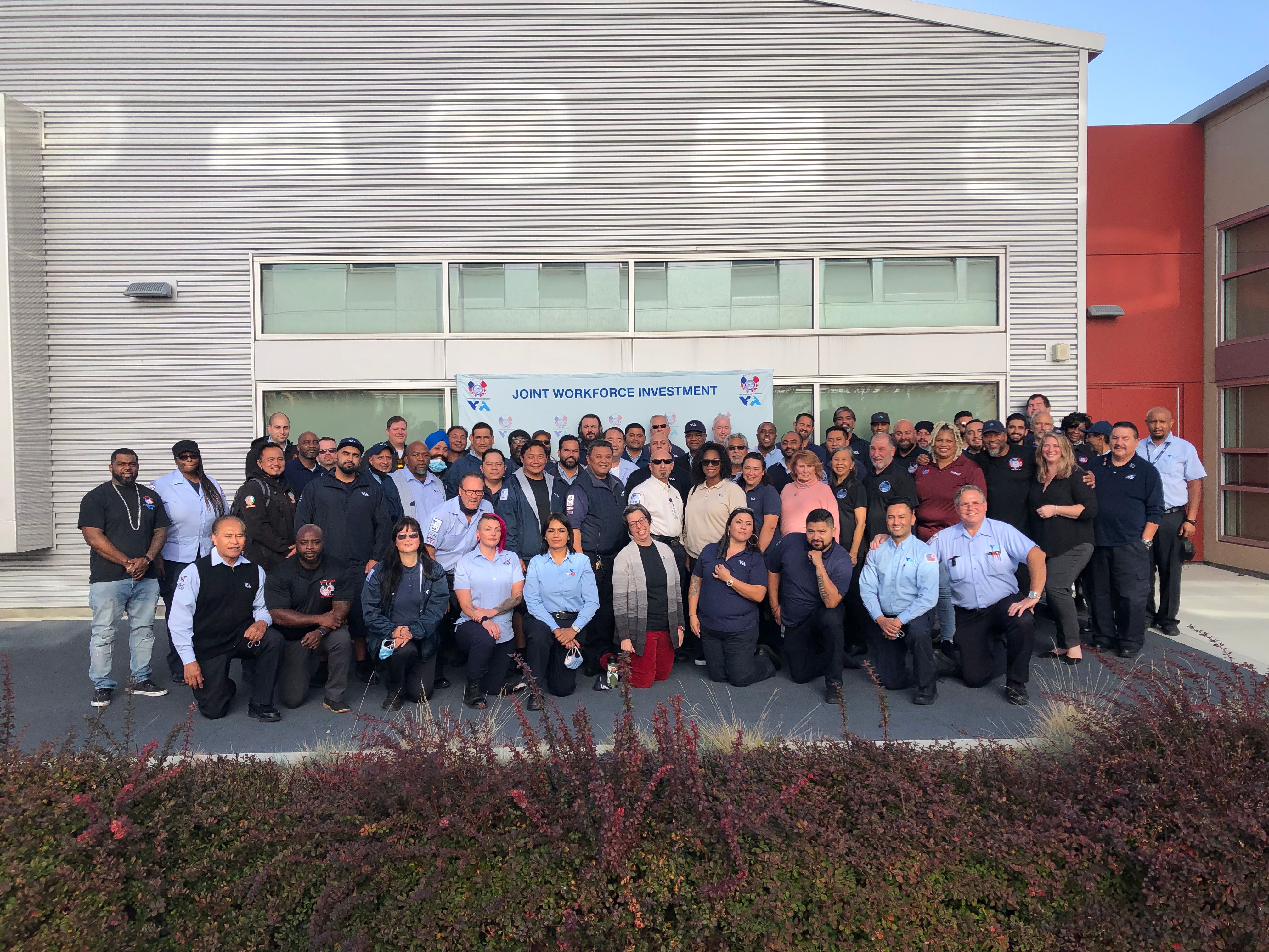 Group photo of several people standing or posing in front of a banner reading "Joint Workforce Investment"