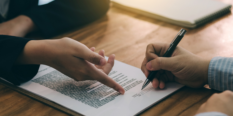 A worker signs an employment contract while the employer points to the signature area.