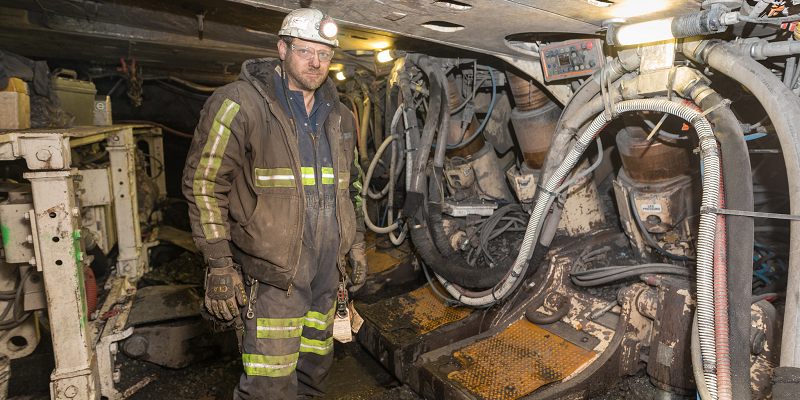 A coal miner covered in dust works inside an underground mine.