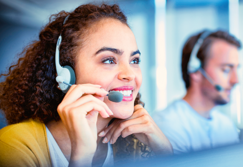 A woman wearing a headset smiles while working at a call center.