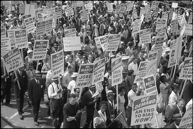 Black and white photo from the Library of Congress shows demonstrators marching in the street holding signs during the March on Washington, 1963.