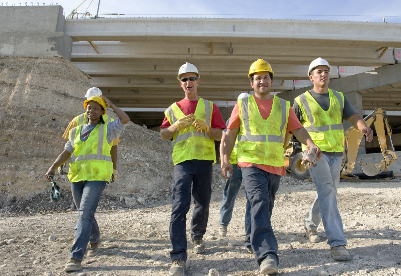 Construction workers in safety gear walk away from a construction site.