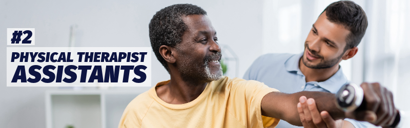 A younger man helps an older man with a physical therapy exercise involving a small hand weight.