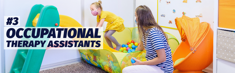 A woman coaches a preschool-age girl through a play area that includes a ball pit and small slide.