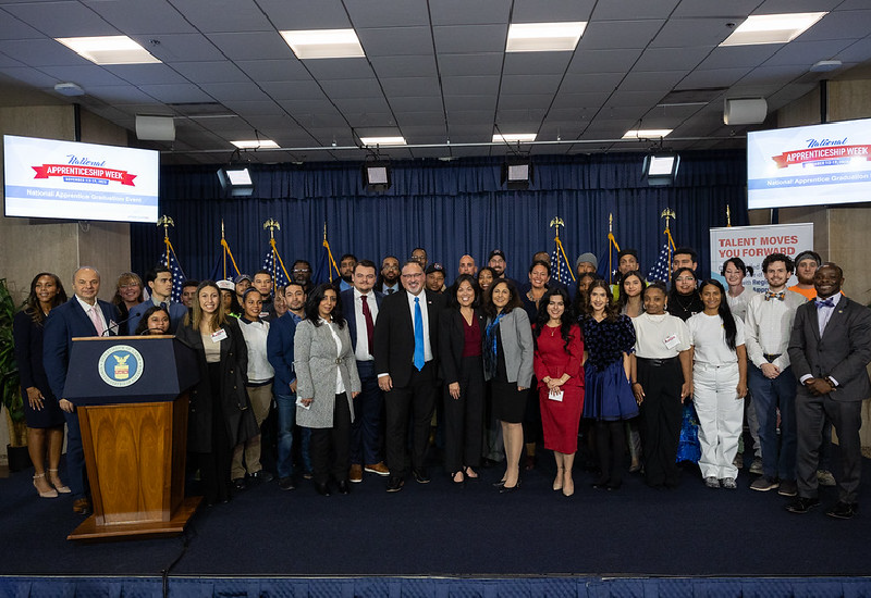 Secretary Su, Secretary Cardona, government officials, students and others crowd together on a stage for a group photo.