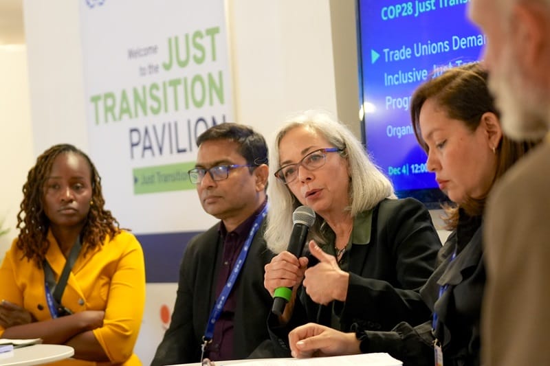 Thea Lee speaks while holding a microphone during a panel discussion with several other people.