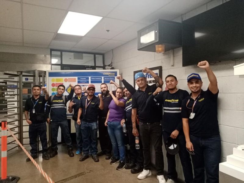Several workers raise their fists in the entrance to a workplace indoors.
