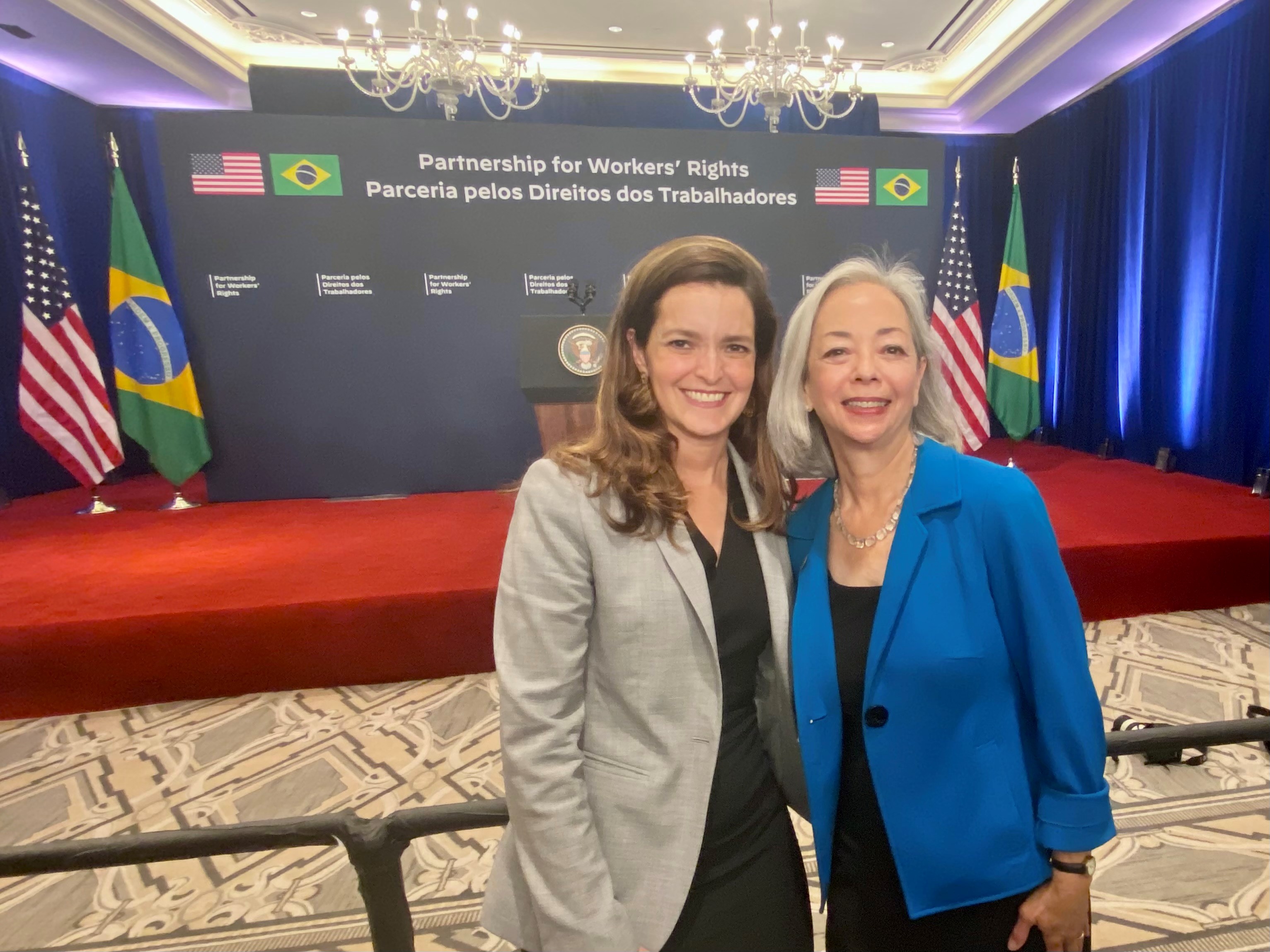 Thea Lee and Special Representative for International Labor Affairs Kelly Fay Rodriguez stand in front of the stage that reads,