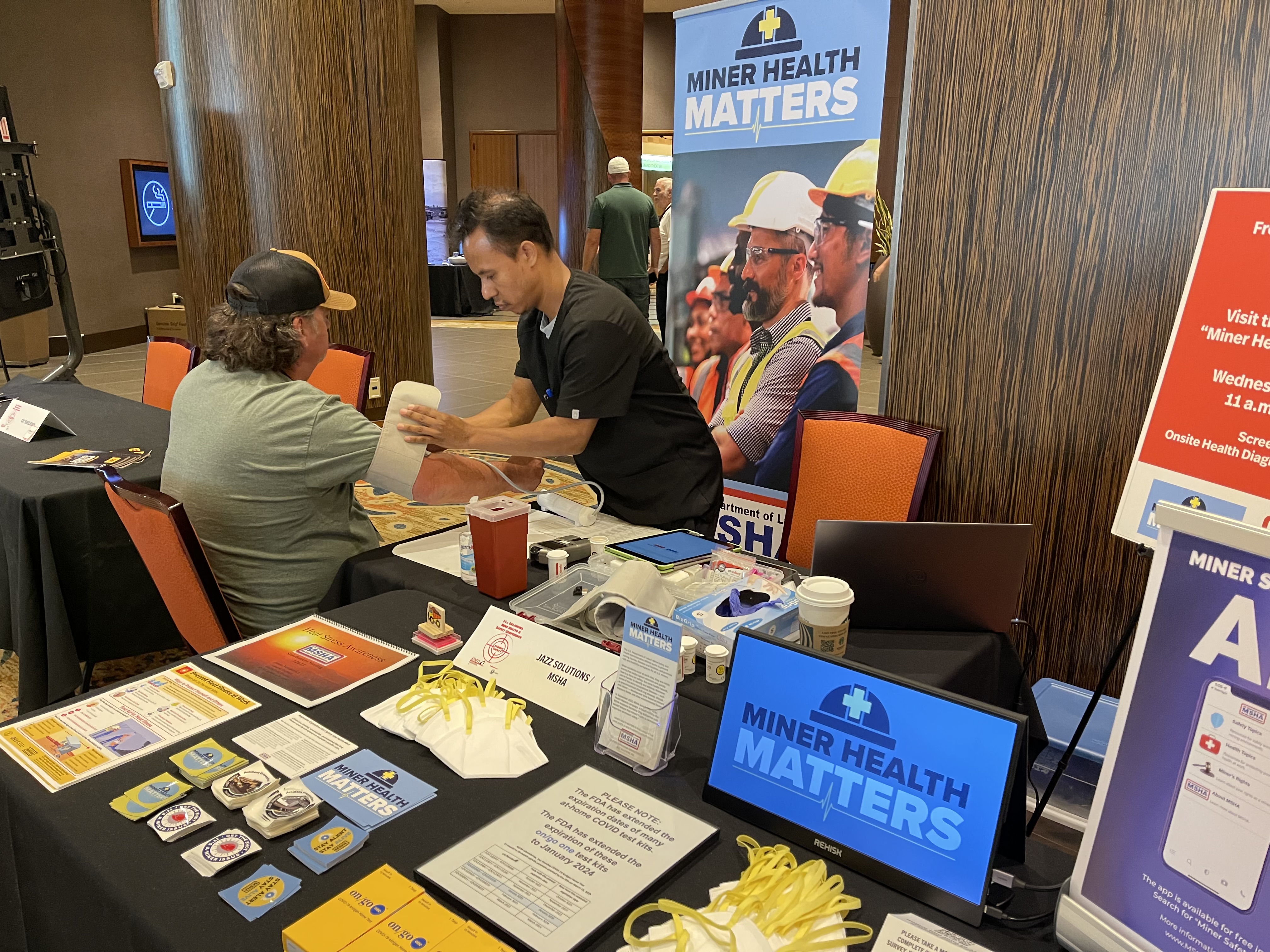 A nurse puts a blood pressure cuff on a miner at a booth with a