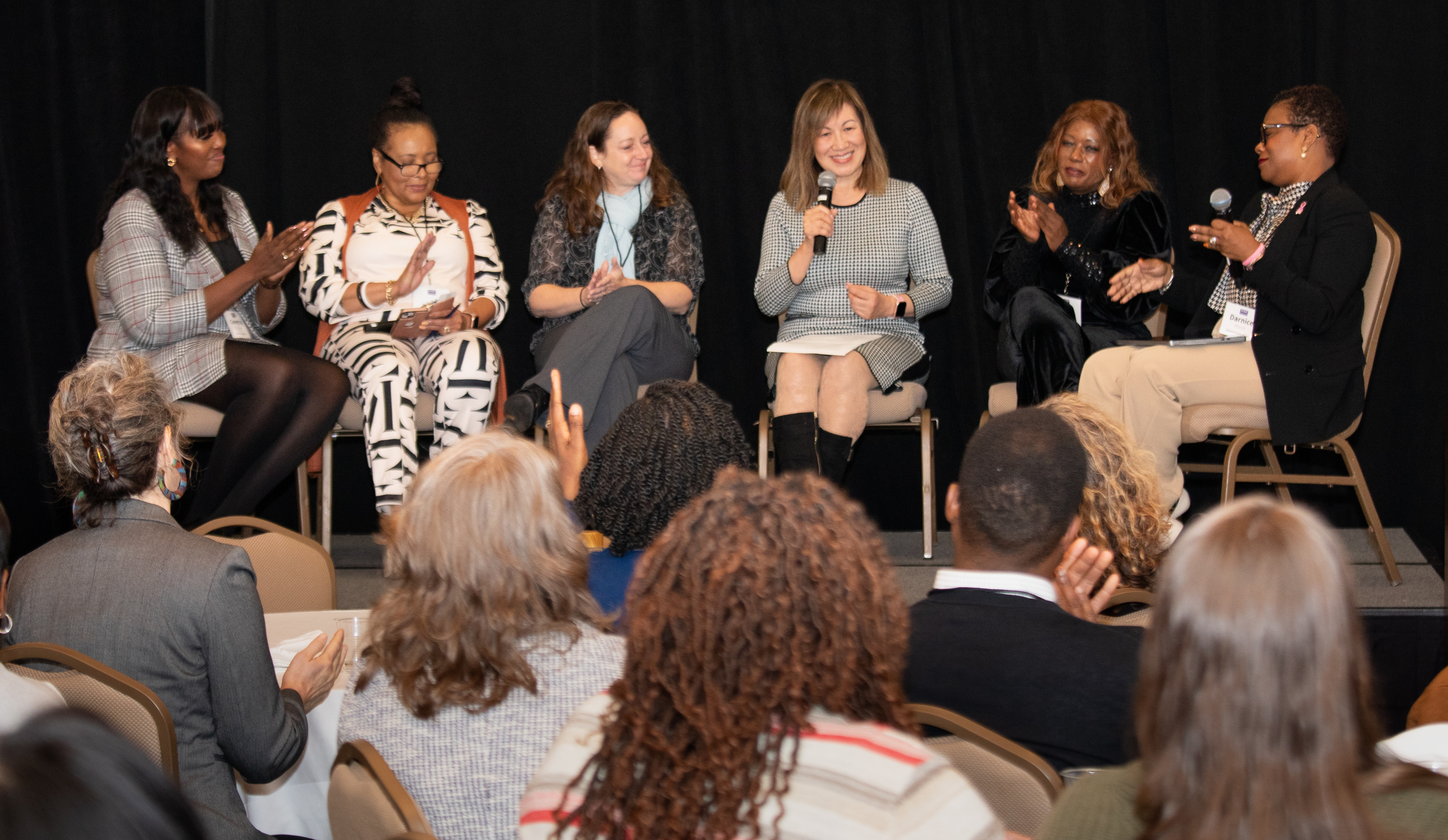 Six women sit in chairs on a stage for a panel discussion.