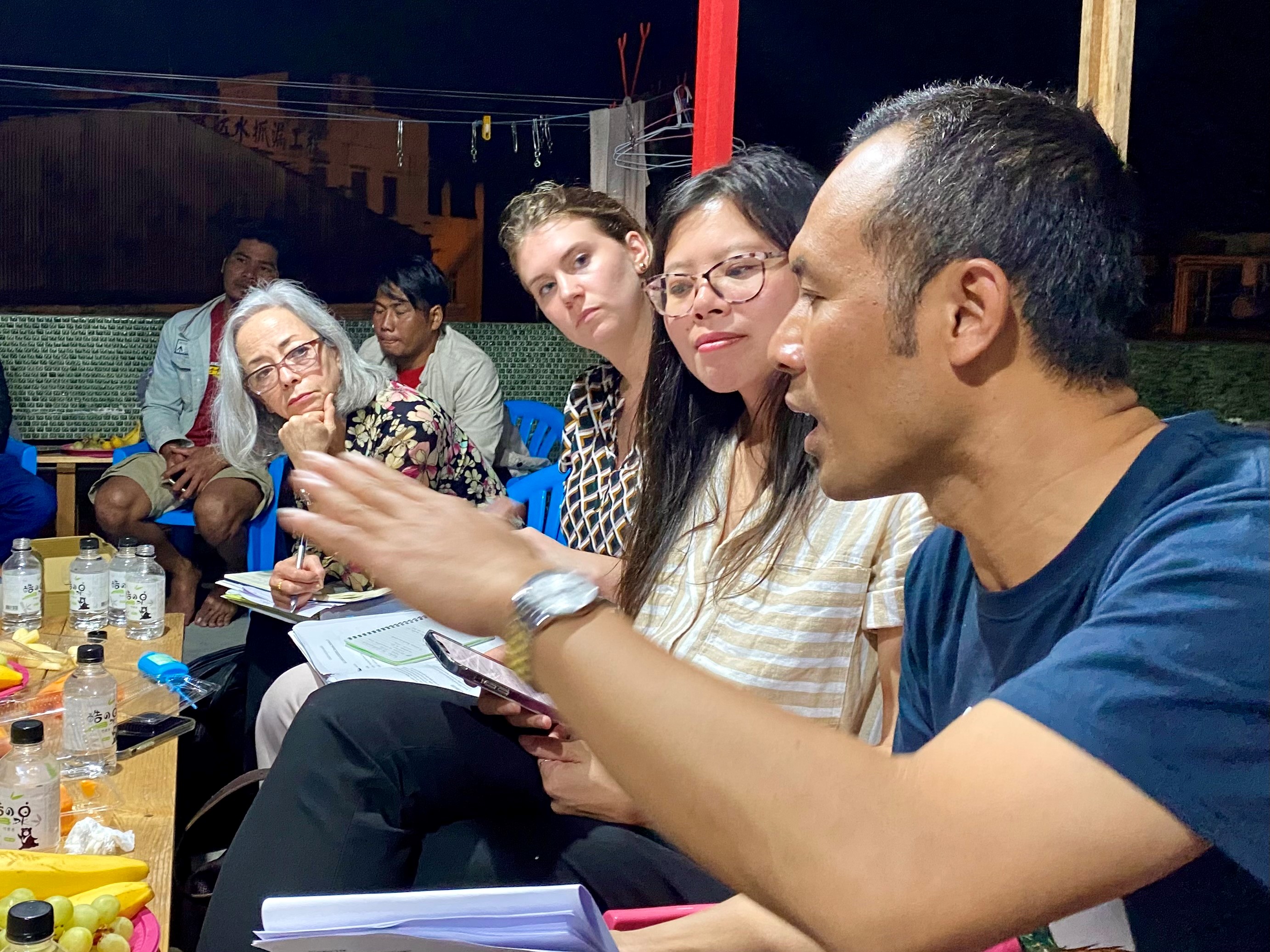 Several American females sit around a table outdoors with members of an Indonesian migrant fishers organization.