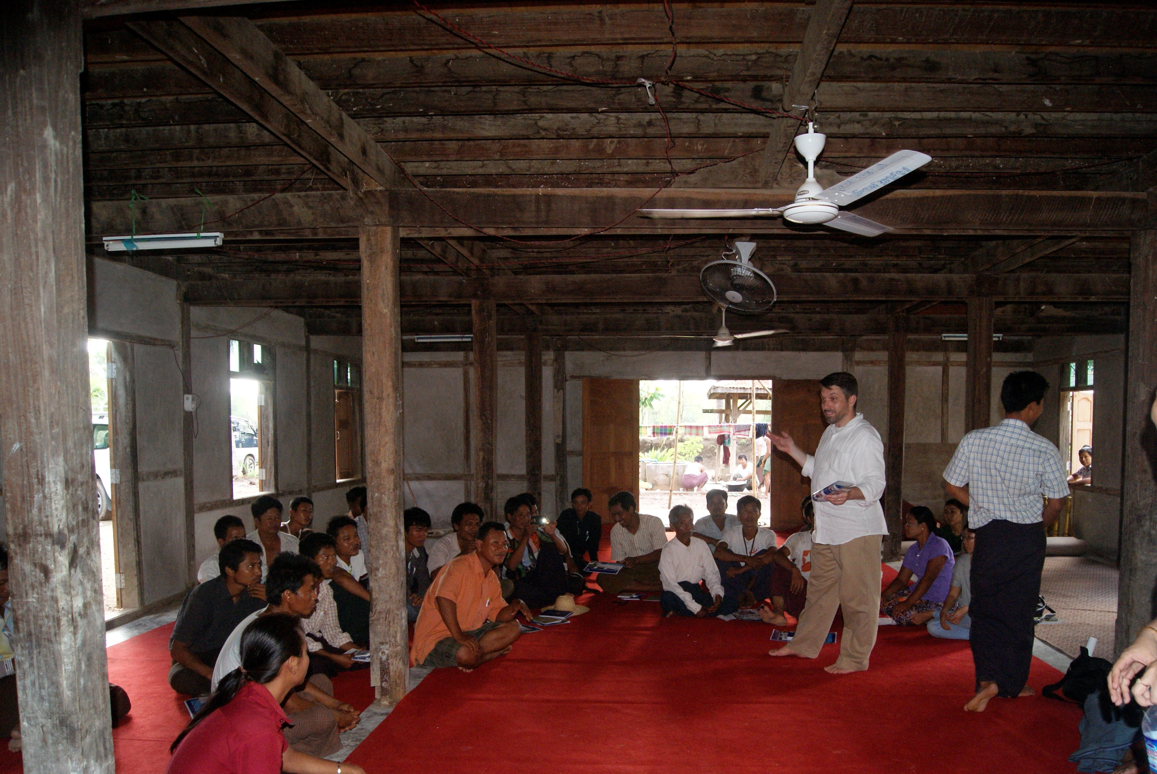 An American male stands in a room full of seated workers, sharing information on workers' rights.