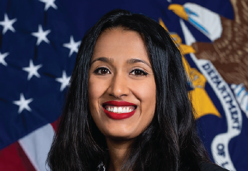 Image of a brown woman with long black hair who is smiling in front of the American and DOL flags.