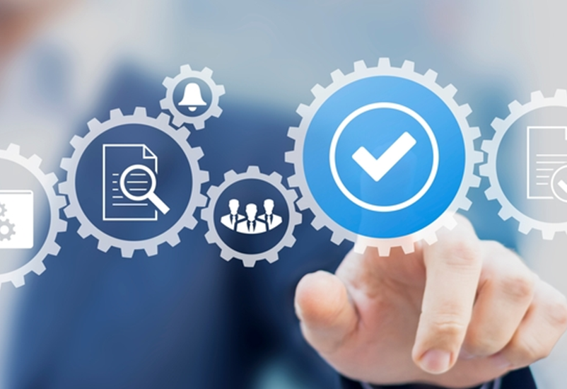 A person in a business suit taps on a floating icon of a checkmark. Other icons hovering in the air depict gears, documents, people collaborating and other work-related imagery.