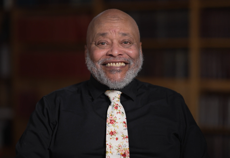 Close-up of Rob Robinson, a Black man wearing a dark shirt and a tie that has a flower pattern.