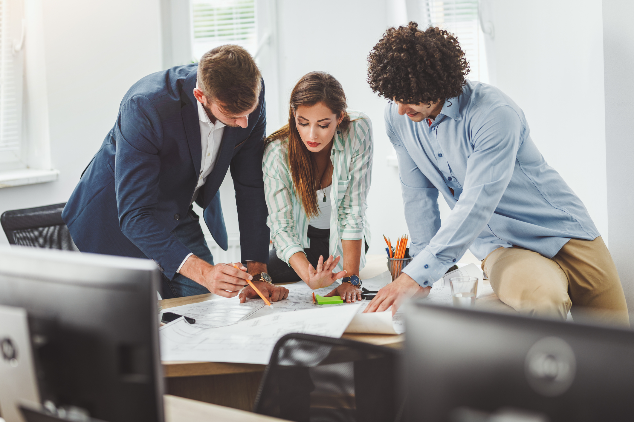 Three office workers lean over a table, examining a file